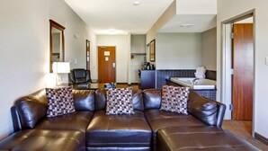 A modern hotel room with a leather sofa, a small desk, a chair, a bathroom with a bathtub, and a mirror. - Tisdale Canalta Hotel (Tisdale)