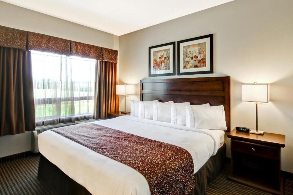 A hotel room with a large bed, two bedside lamps, a nightstand, and two framed pictures on the wall.