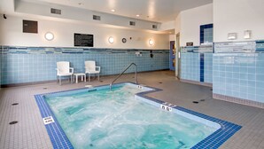 A swimming pool with a tiled deck, a hot tub, and two white chairs. - Tisdale Canalta Hotel (Tisdale)