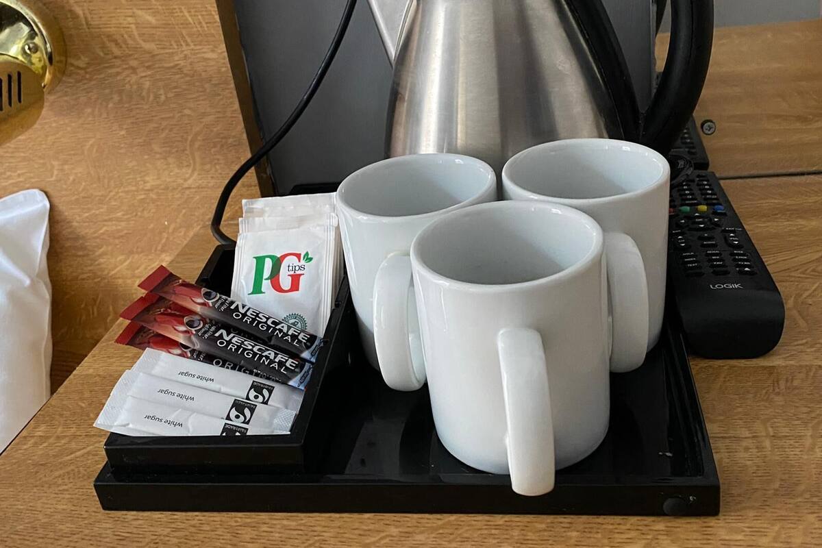 A tray with four white mugs, a black coffee pot, a remote control, and packets of PG tips and Nescafe Original coffee.