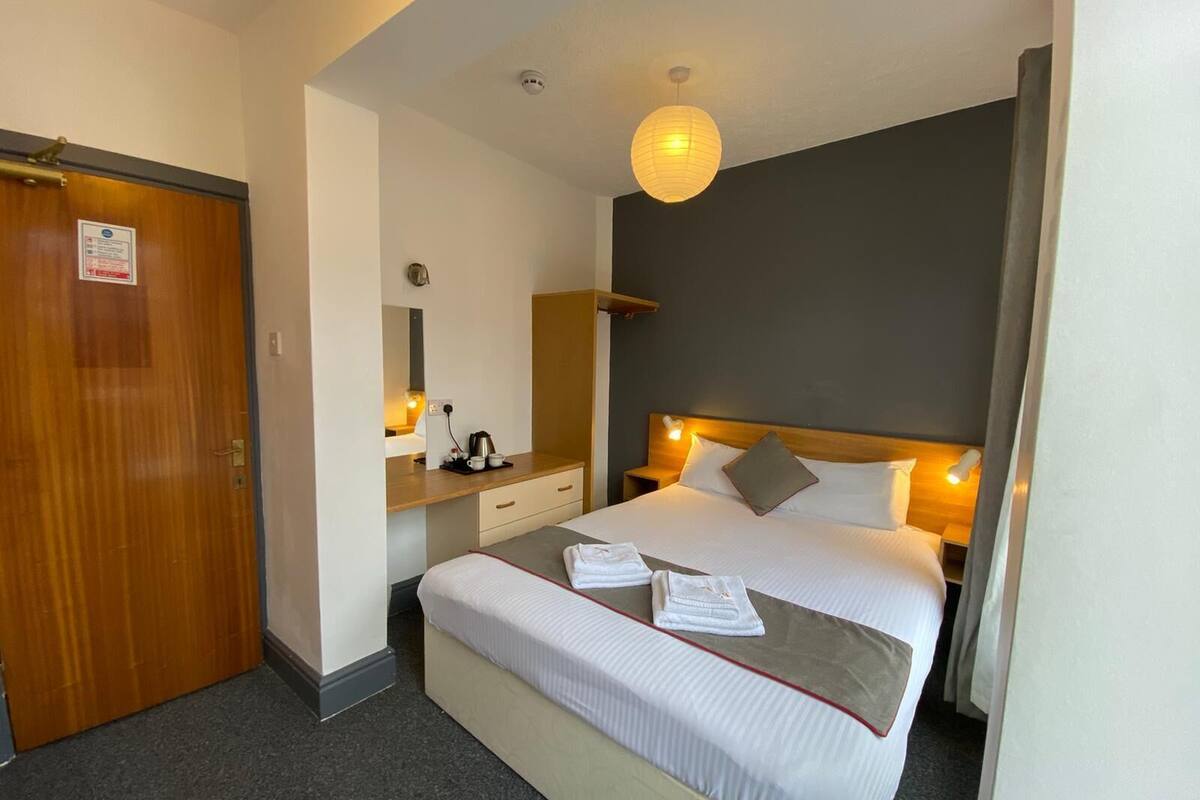 A hotel room with a bed, bedside table, lamp, and a wooden door.