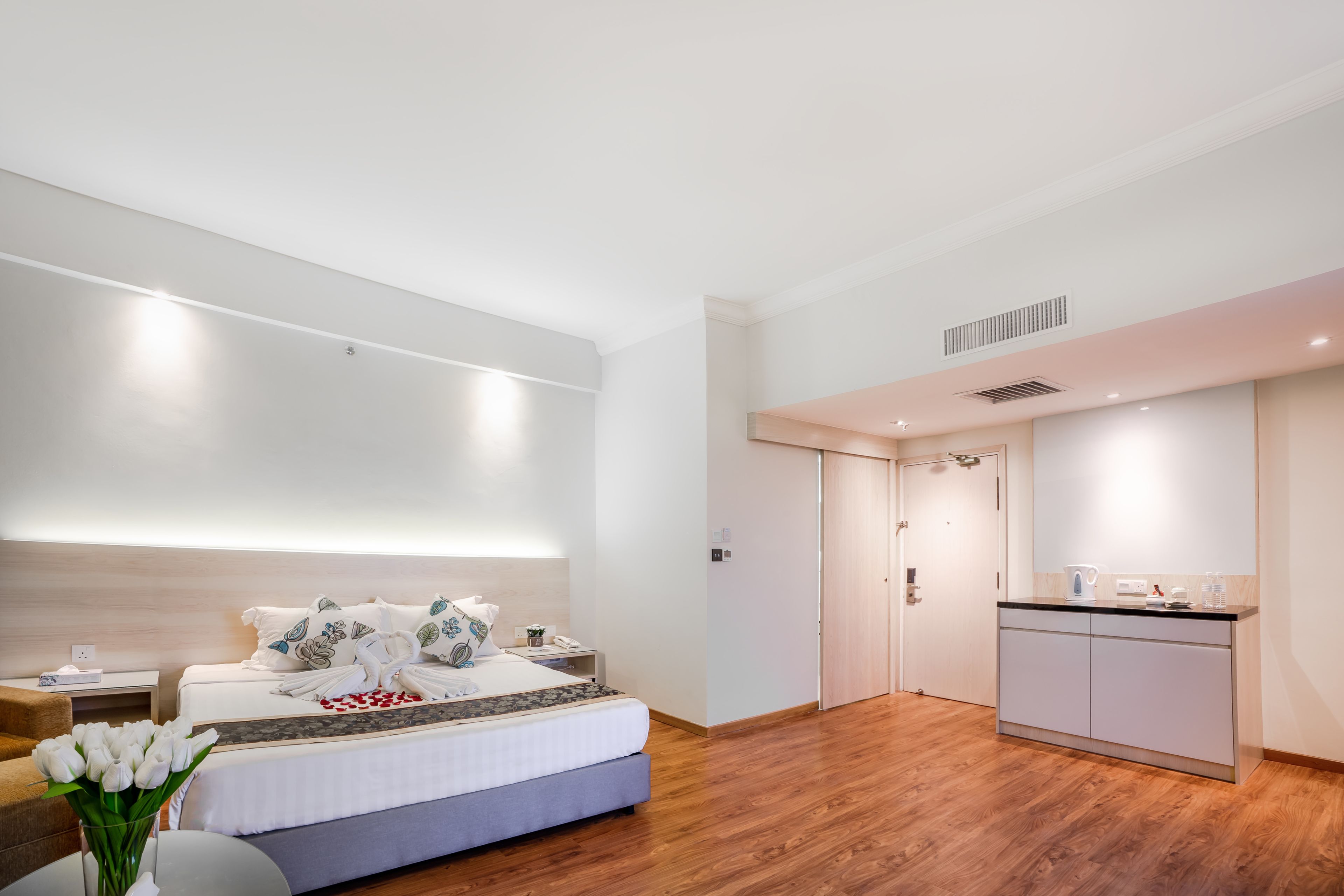 Una habitación de hotel moderna con una cama grande, una mesita de noche y una pequeña kitchenette.