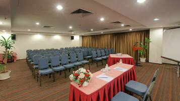 Una sala conferenze con file di sedie, un tavolo con tovaglia rossa e uno schermo per proiettore.