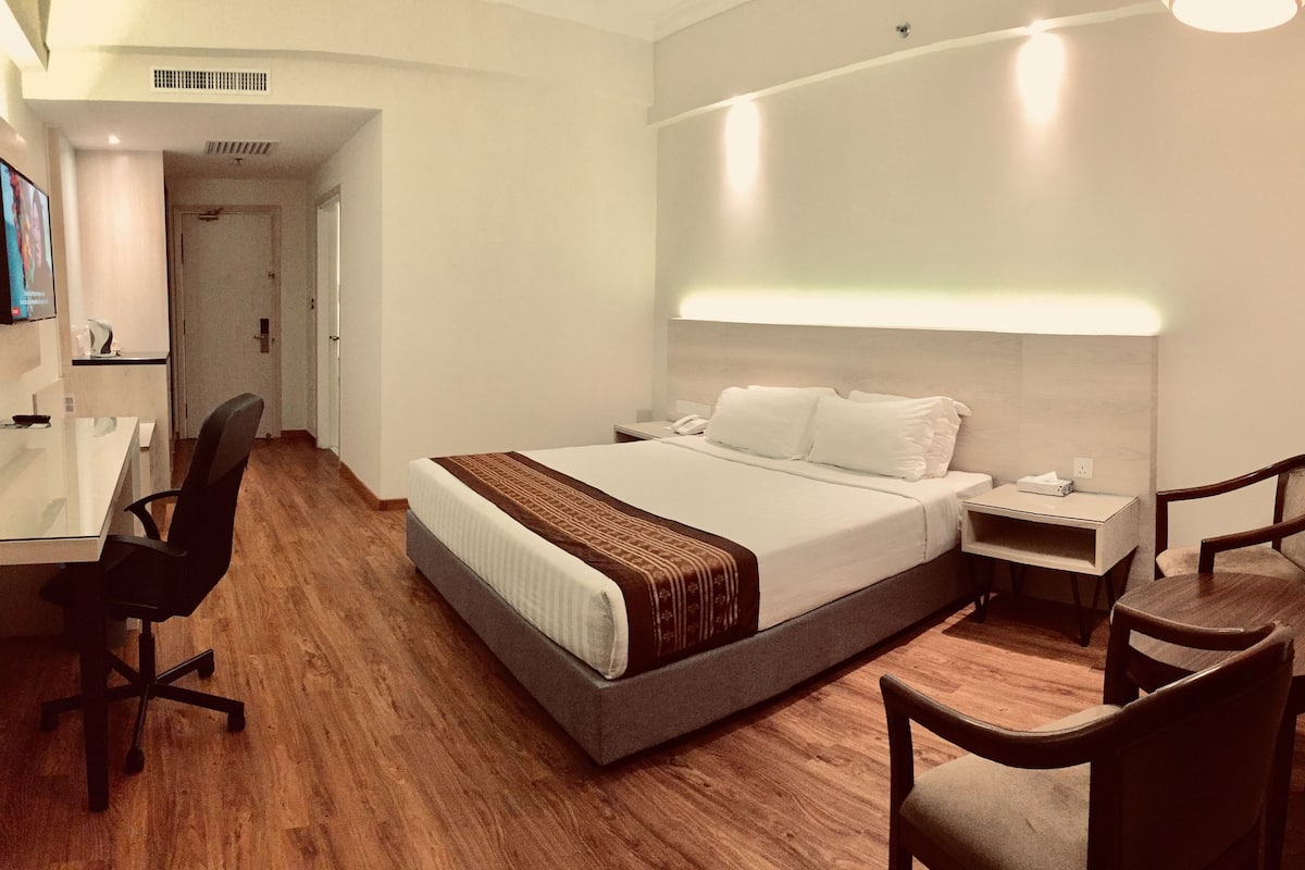 A hotel room with a large bed, bedside tables, a desk, and two chairs.