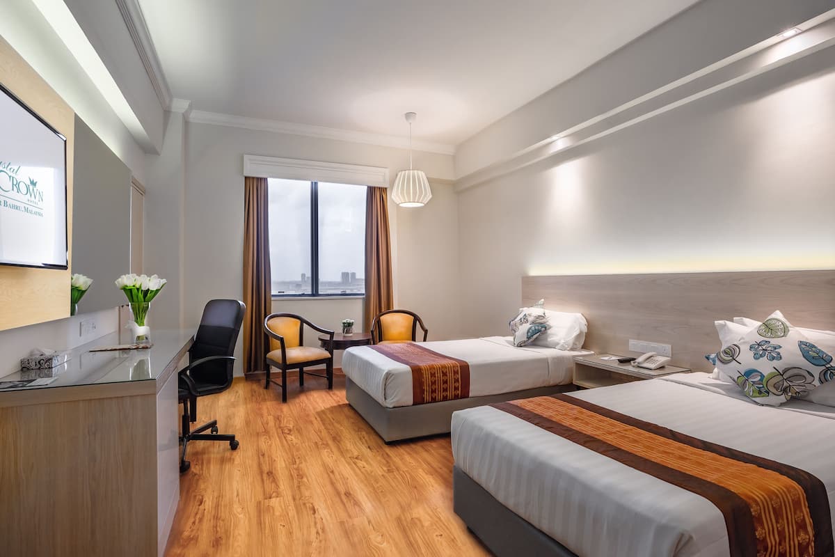 A hotel room with a desk, two beds, a chair, a small table, and a window with curtains.