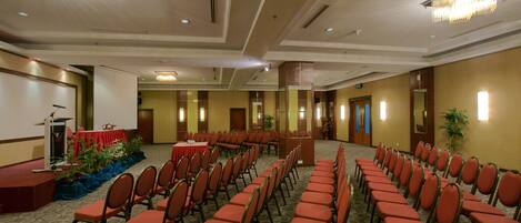 Un salón de conferencias con filas de sillas, un escenario con un atril y piso alfombrado.