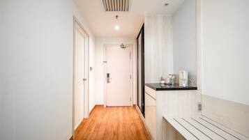 A narrow hallway with wooden flooring, a white door at the end, and a kitchenette area with a countertop and appliances.