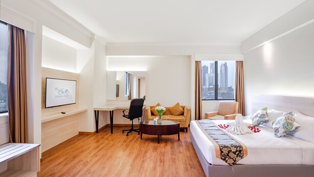 Habitación de hotel con cama, sofá, escritorio y silla. Se ve una ventana con vistas a edificios.