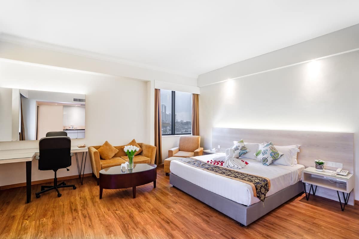 A modern hotel room with a large bed, a desk, a sofa, and a small table.