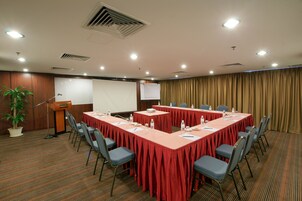 A conference room with a long table, chairs, a podium, and a projector screen.