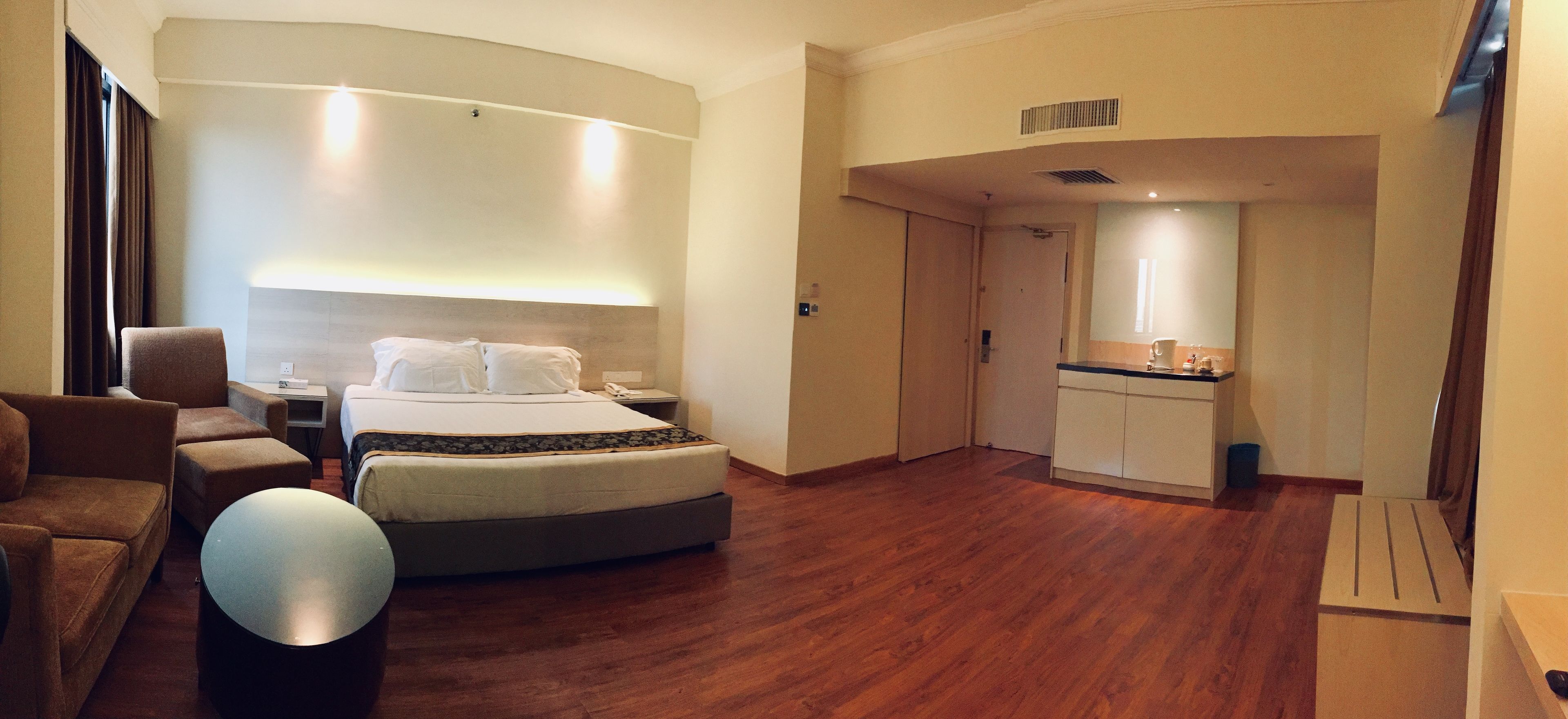 A hotel room with a bed, a sofa, a round table, a kitchenette, and a bathroom.