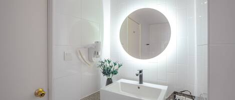 Un baño moderno con un lavamanos blanco, un espejo redondo y una planta pequeña en la encimera.