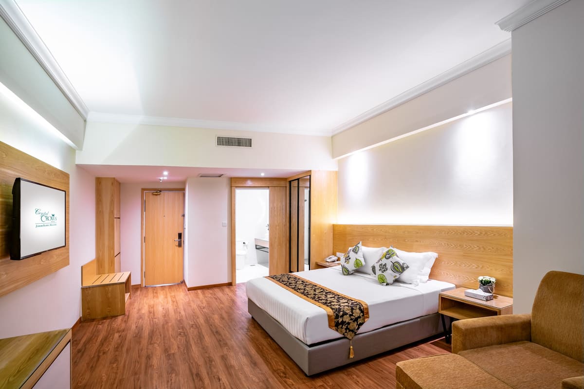 A hotel room with a bed, bedside table, chair, and a television on the wall.