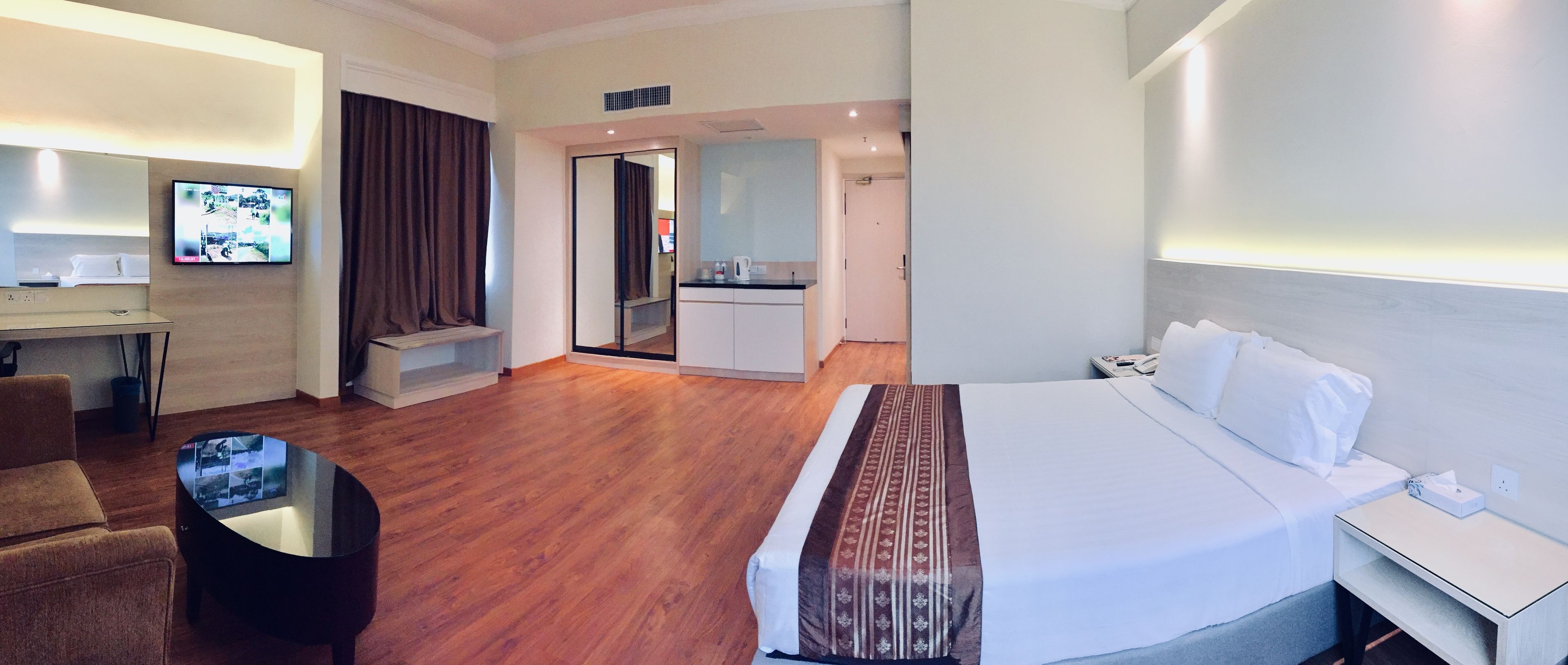 Ein Hotelzimmer mit Bett, Schreibtisch mit Fernseher, Sitzecke und einer Küchenzeile.