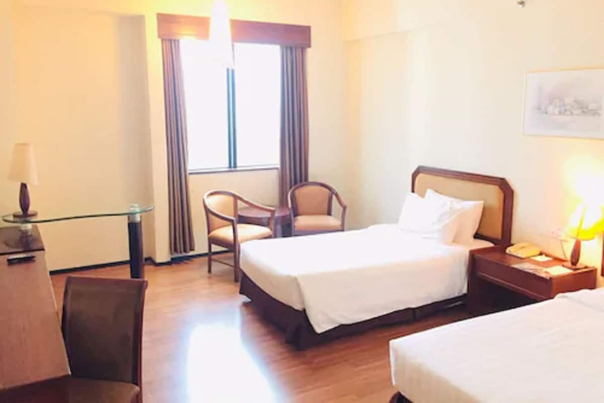 A hotel room with a bed, a chair, a desk, and a nightstand with a lamp.