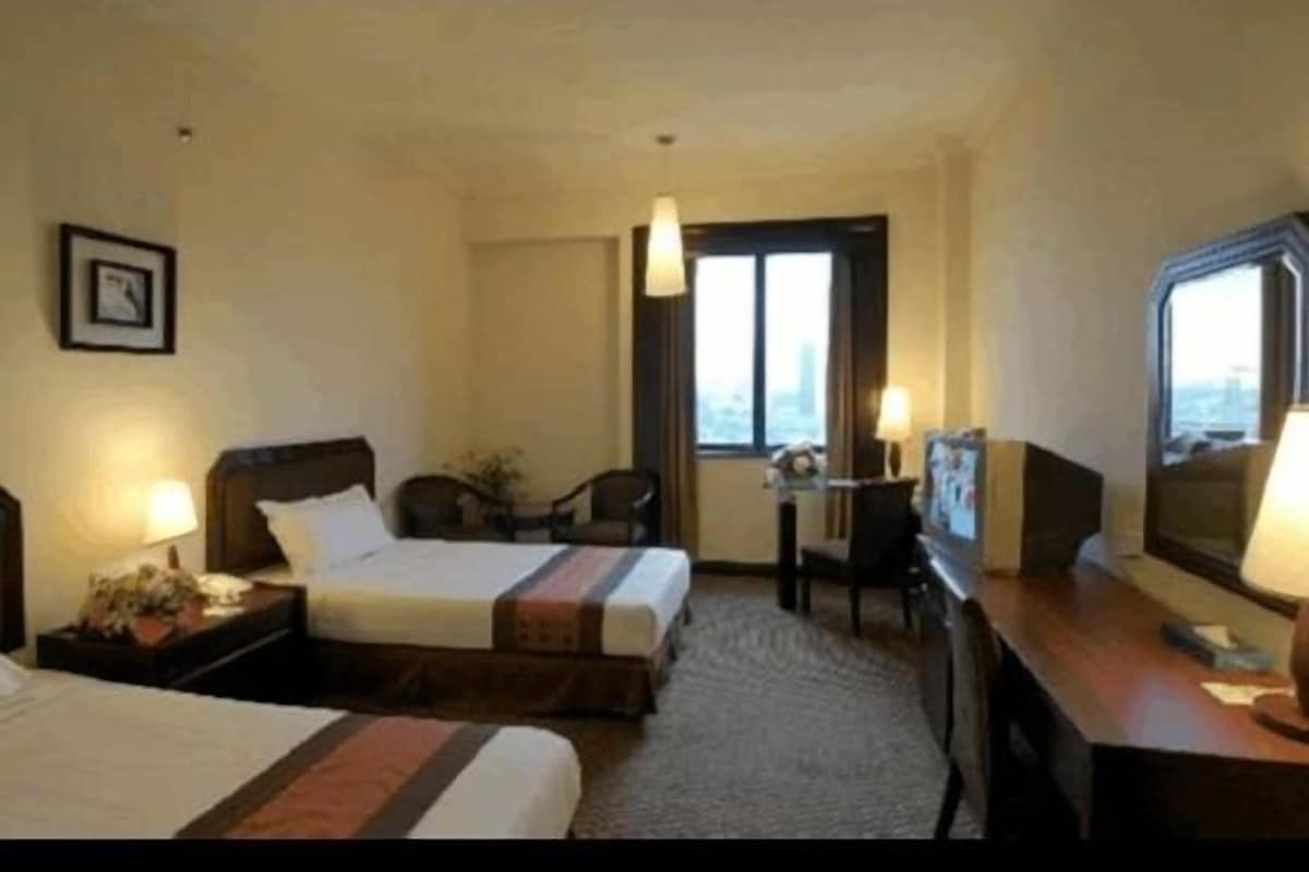 Habitación de hotel con dos camas, un escritorio, una silla, un televisor y una ventana con vista a la ciudad.