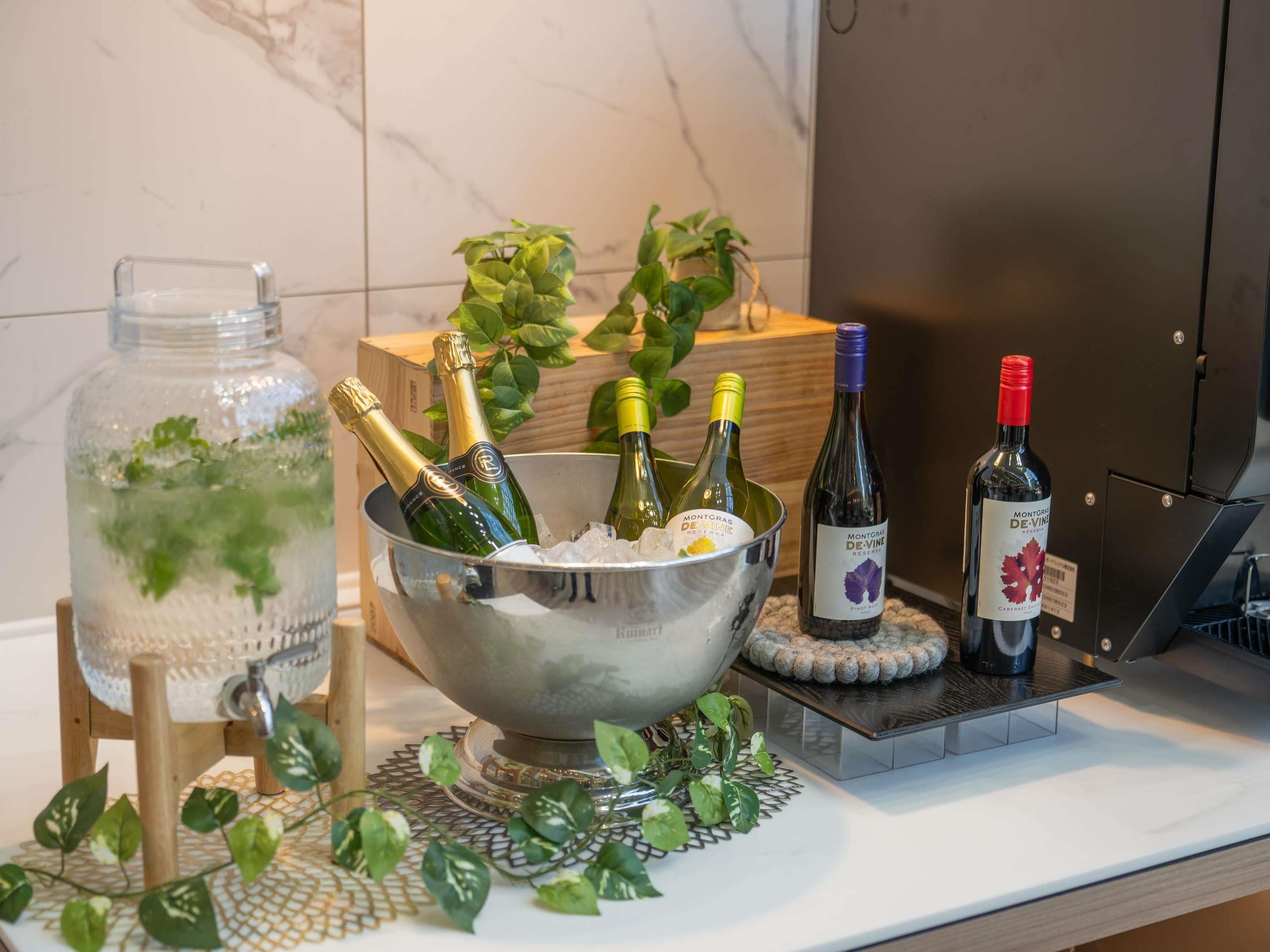 A kitchen counter with a metal bowl containing champagne bottles, a wine bottle, and a glass jar with greenery.
