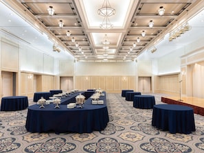 Une grande salle de conférence équipée d’une longue table, de tables rondes et d’une scène avec un microphone.