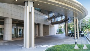 Un bâtiment moderne doté d’un toit incurvé, de grandes colonnes et d’un espace de stationnement.