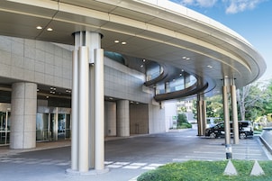 A modern building with a curved roof, large columns, and a parking area.