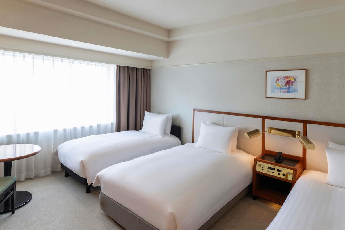 Quarto de hotel com duas camas, uma mesa de cabeceira, um abajur e um quadro na parede.