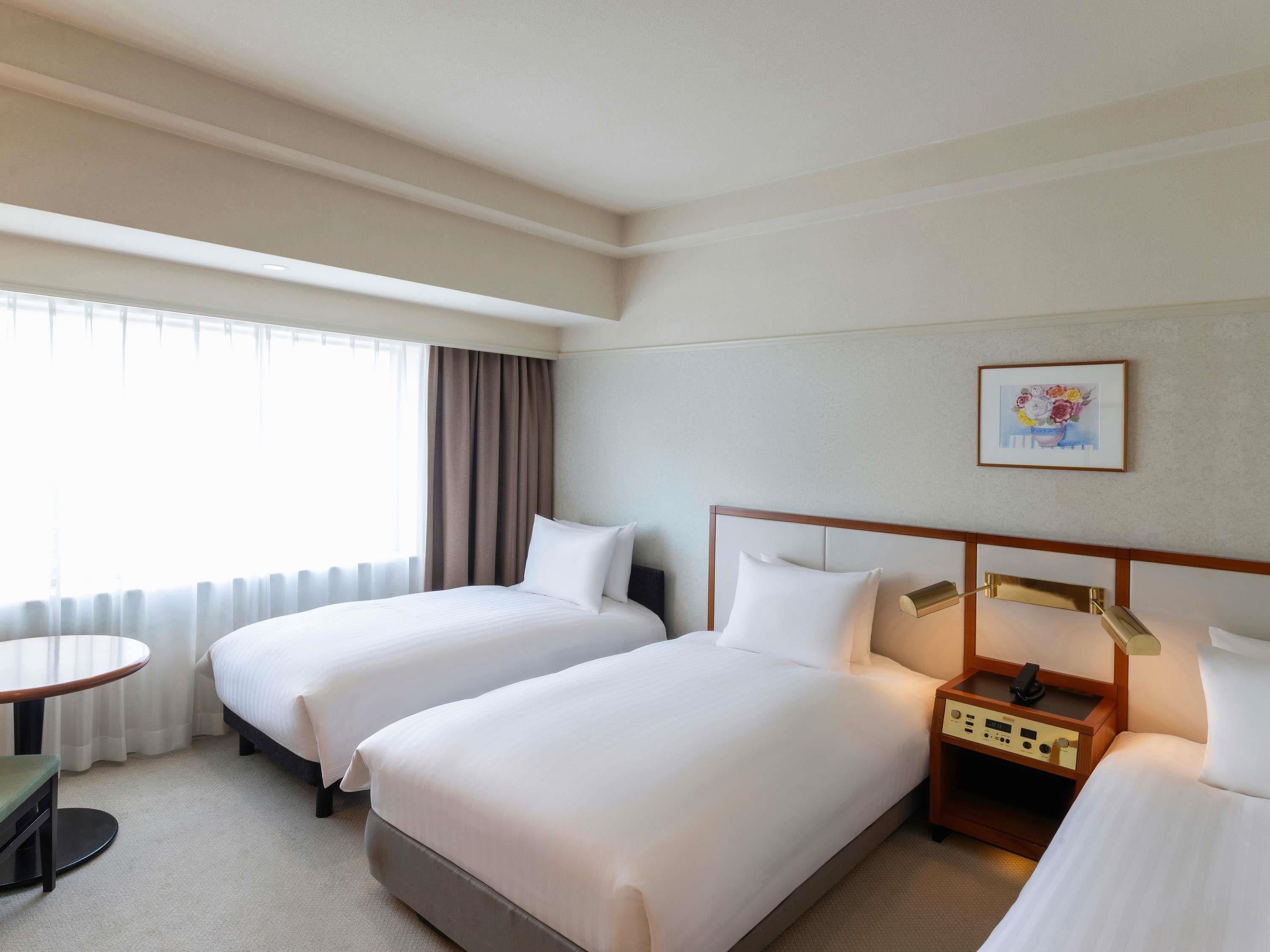 A hotel room with two beds, a bedside table, a lamp, and a painting on the wall.