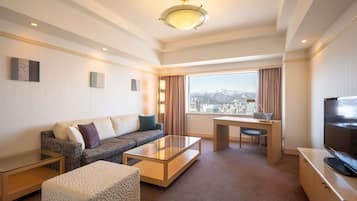 A hotel room with a sofa, ottoman, coffee table, desk, and TV.