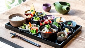 Une variété de plats japonais présentés sur un plateau, comprenant du riz, des légumes et de la viande, accompagnés de baguettes et de petits bols.