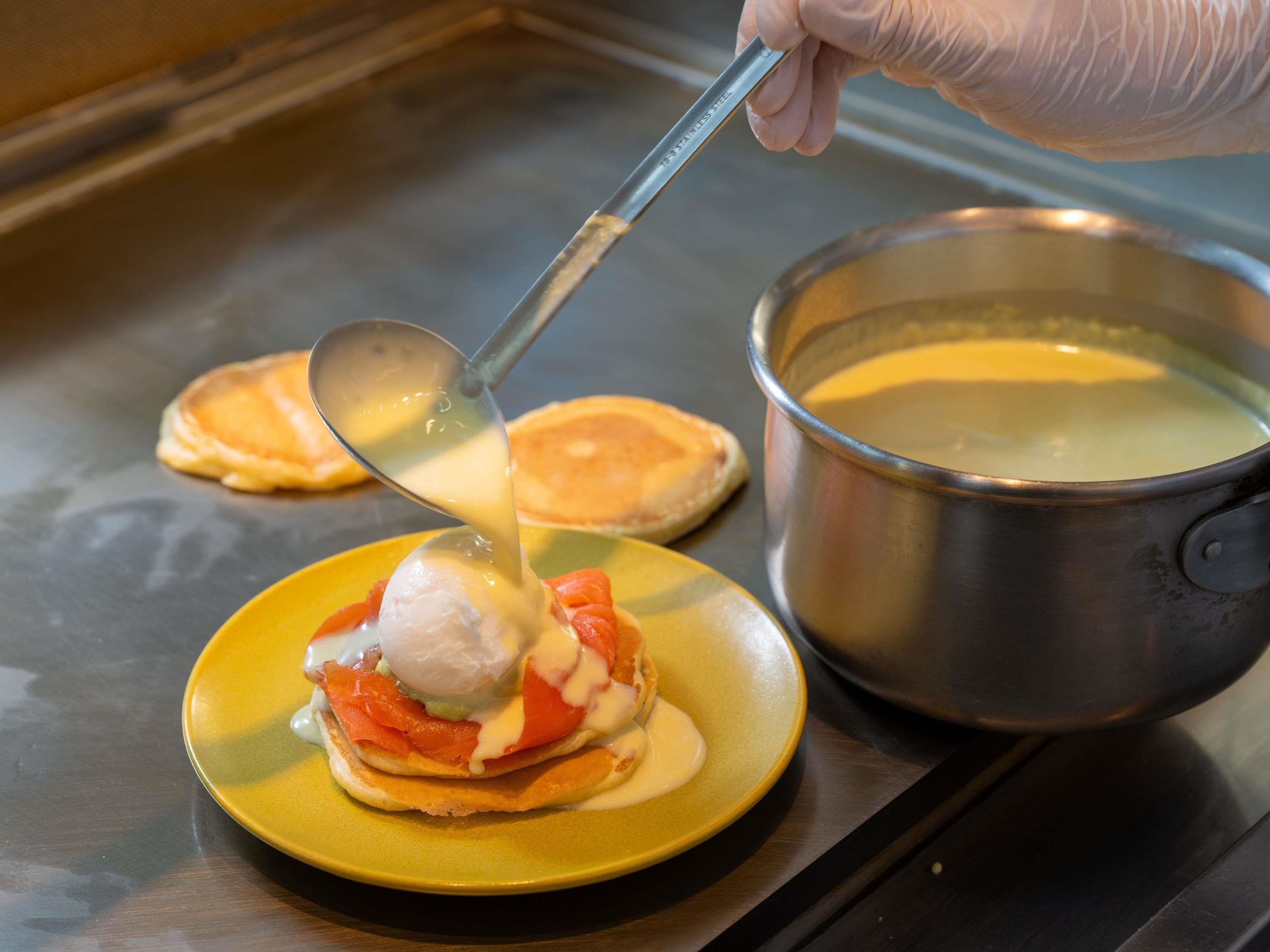 A person pouring sauce onto a dish with pancakes and smoked salmon.