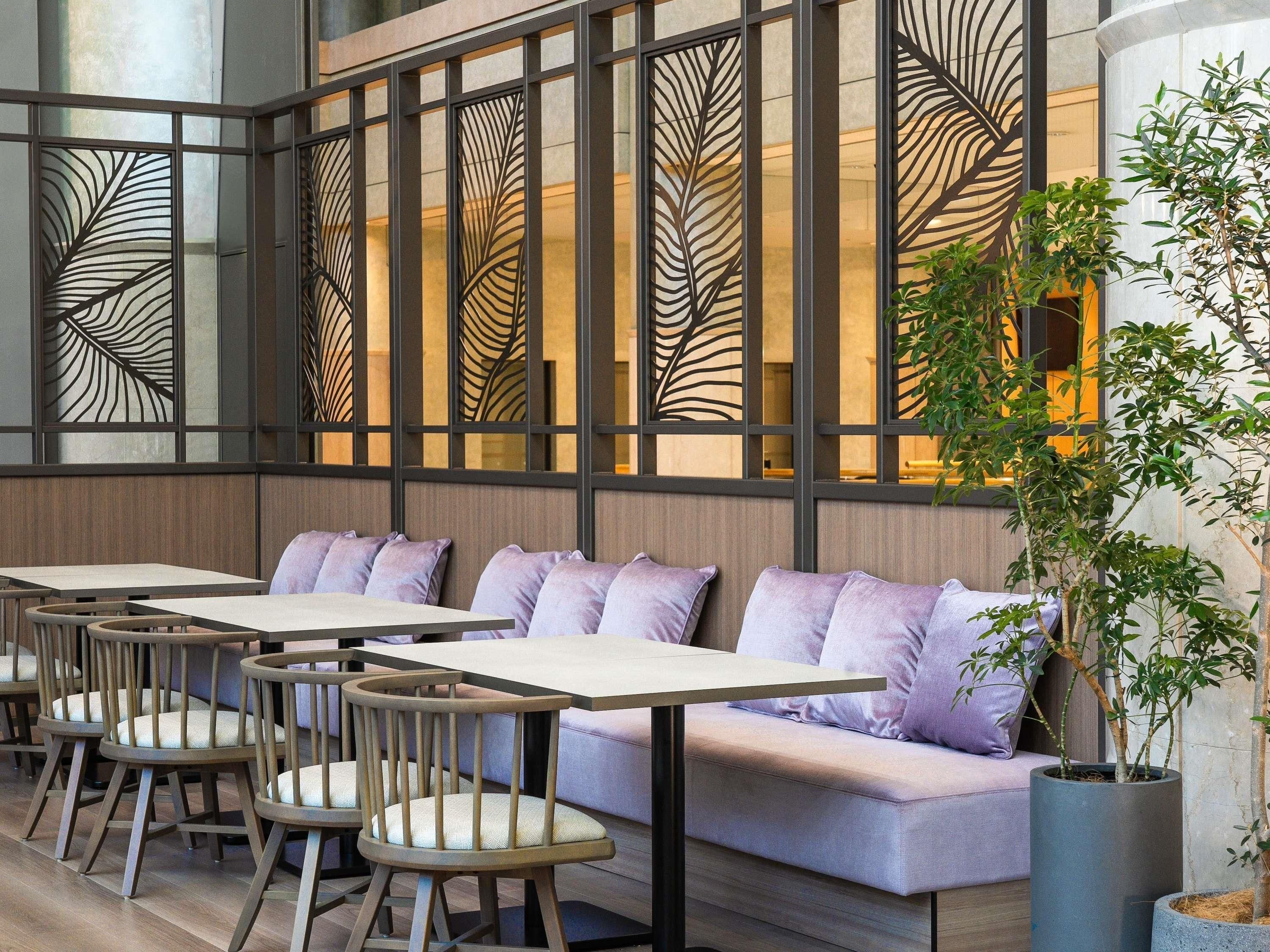 A modern interior with wooden tables and cushioned seating, a decorative partition with leaf patterns, and potted plants.