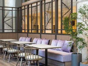 A modern interior with wooden tables and cushioned seating, a decorative partition with leaf patterns, and potted plants. - Grand Mercure Sapporo Odori Park (Sapporo)