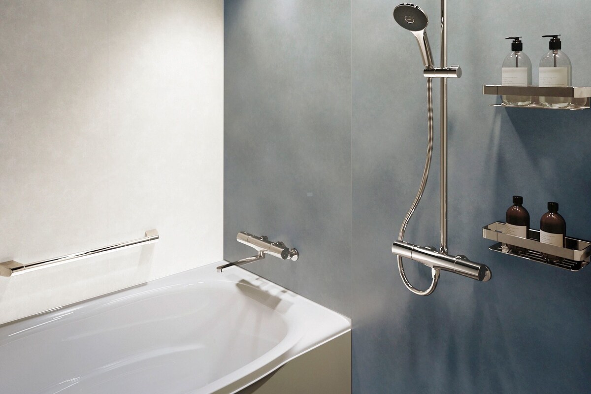 A modern bathroom with a white bathtub, a handheld showerhead, and a wall-mounted shelf with two bottles.