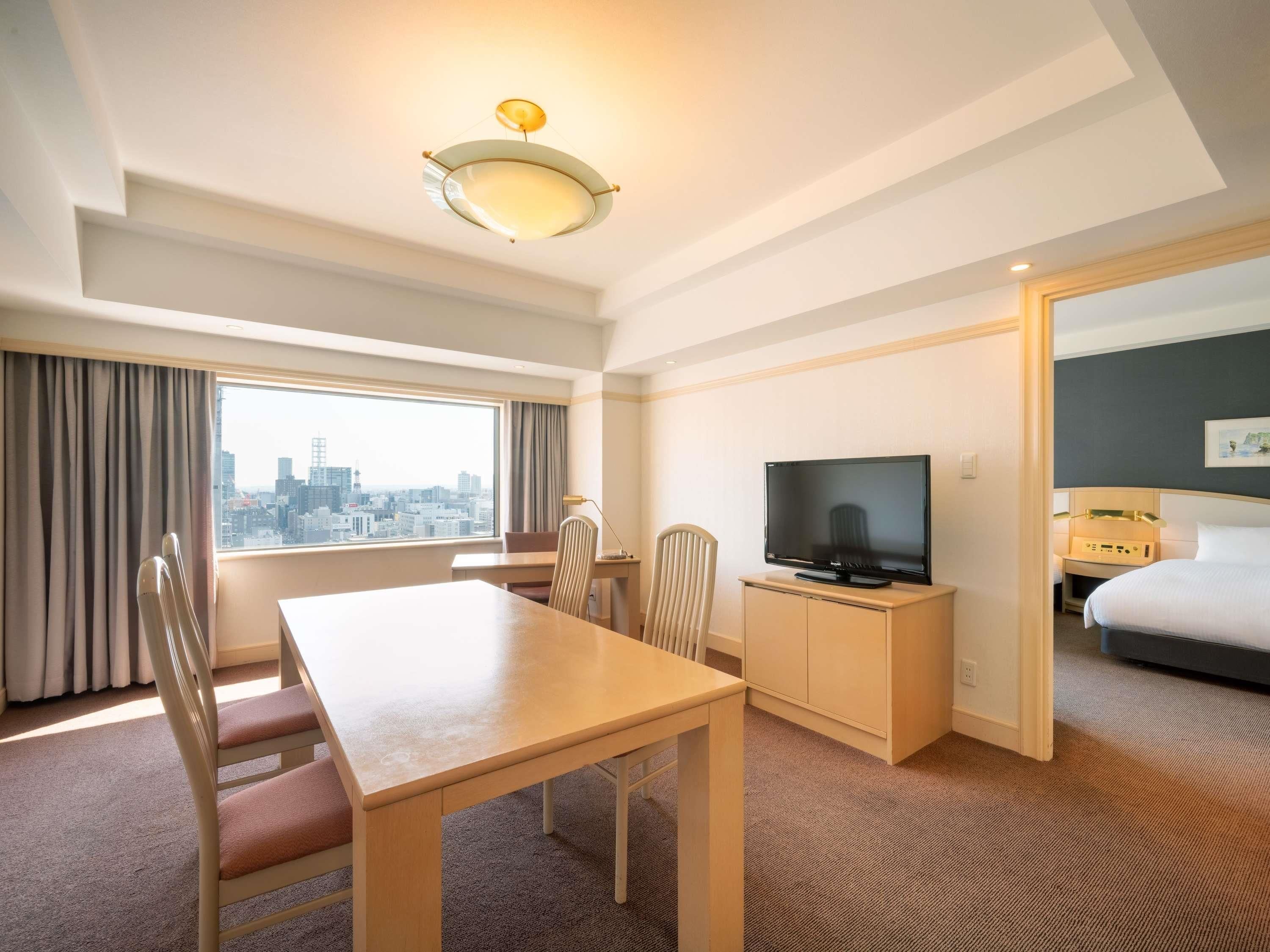 A hotel room with a city view, a dining table, a TV, and a bed.