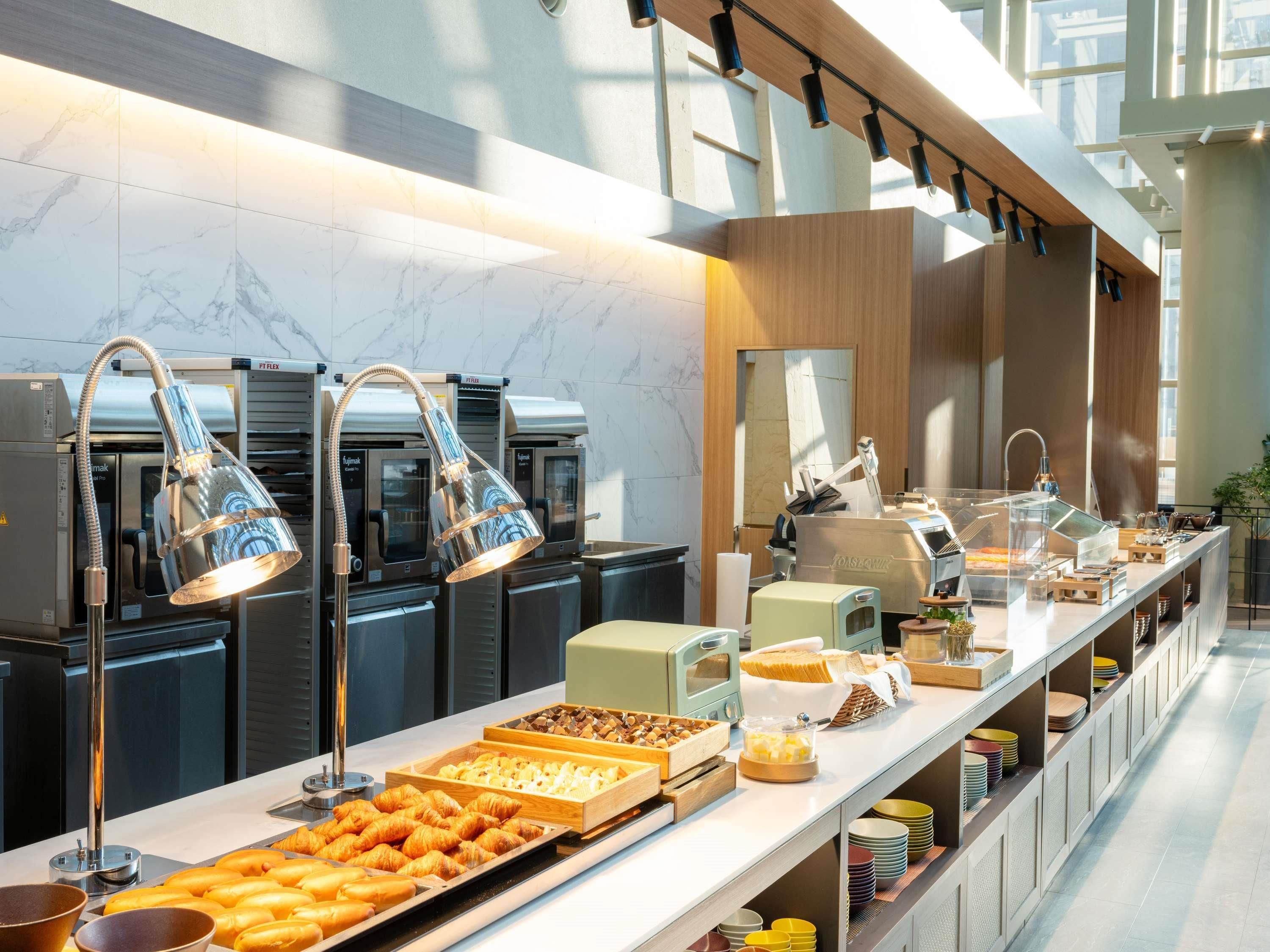 Buffet com diversos alimentos, máquina de café e vitrine de vidro transparente.