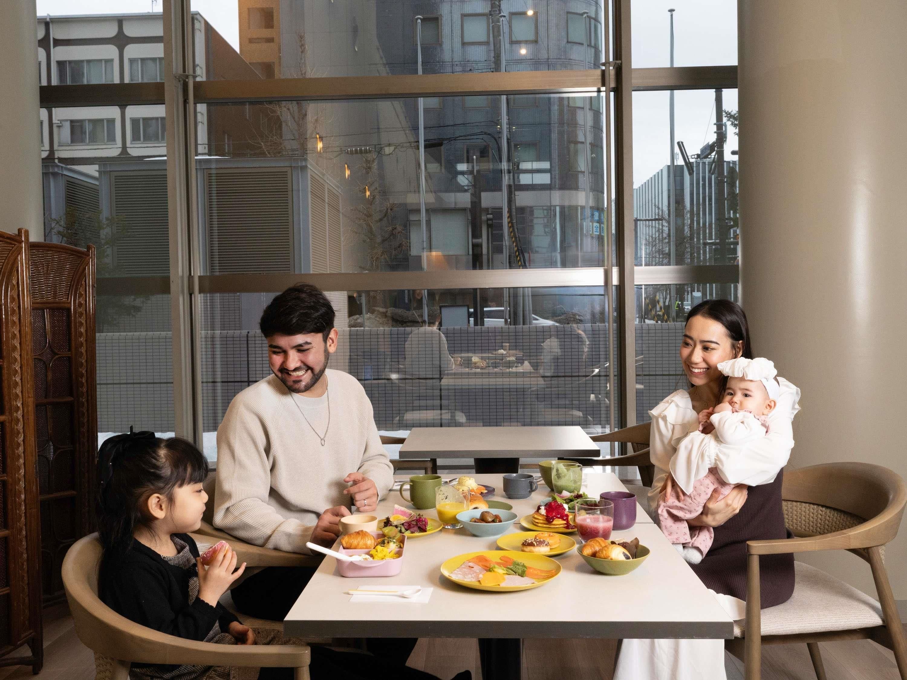 Una familia cenando en una mesa con varios platos, en un interior moderno con ventanas amplias.