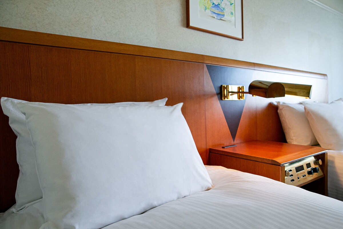 A hotel room with a wooden headboard, a bedside table with a lamp, and a framed picture on the wall.