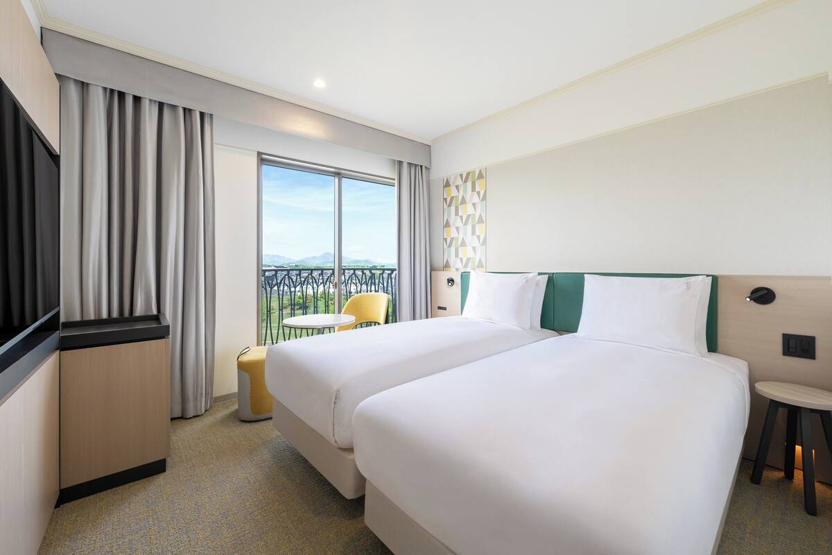 Une chambre d’hôtel avec deux lits, un bureau, une chaise et un balcon avec vue.