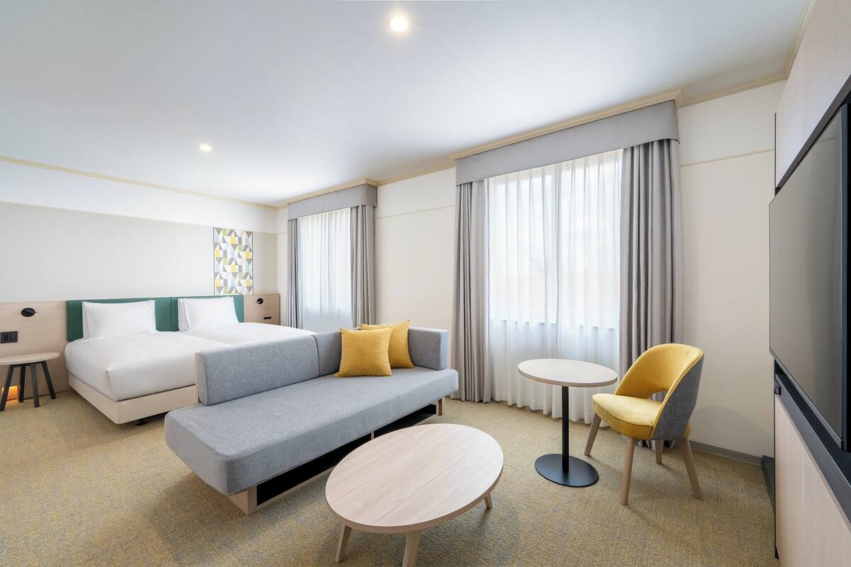 Une chambre d’hôtel avec un lit, un canapé, deux fauteuils, une petite table et un téléviseur.