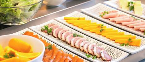 Un bufé con diversos alimentos, incluyendo carnes cortadas, quesos y un tazón de ensalada.