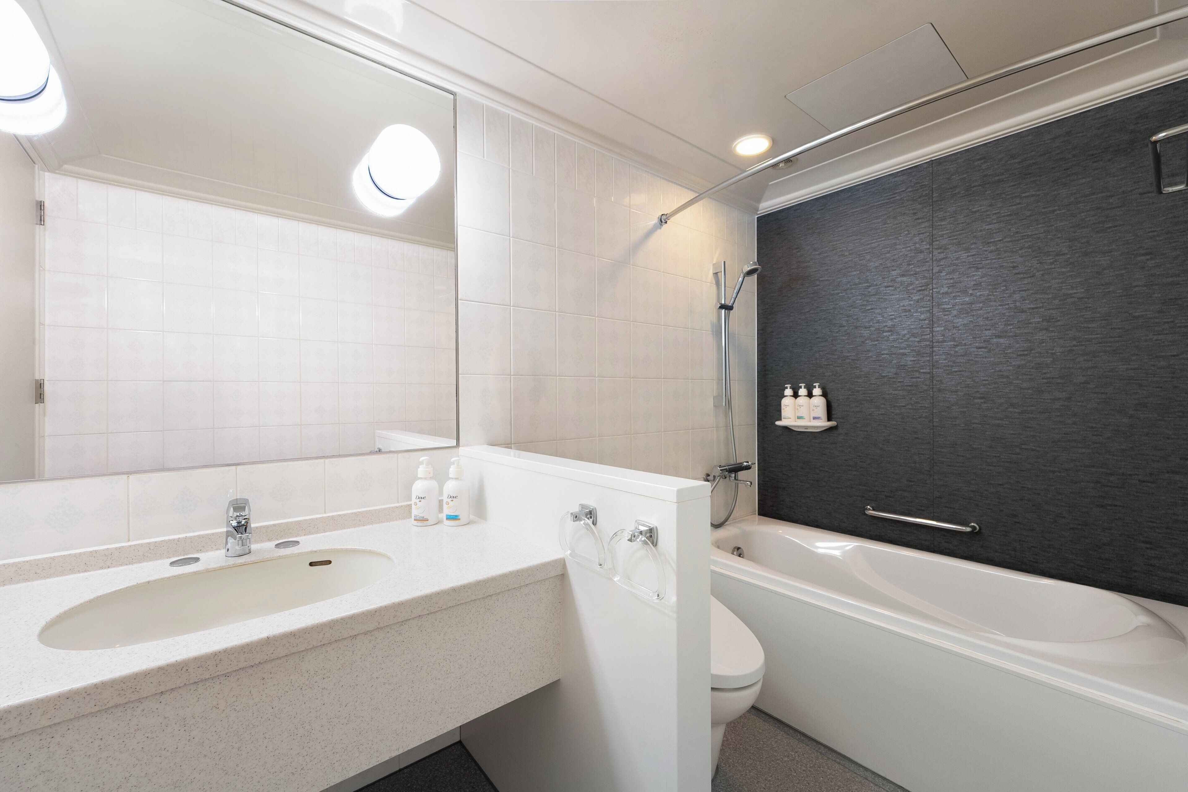 A modern bathroom with a sink, mirror, toilet, and bathtub.