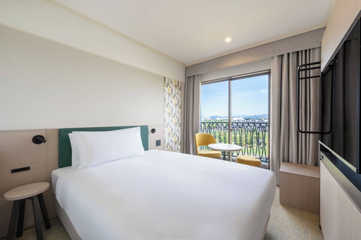 Une chambre d’hôtel avec un grand lit, une petite table ronde, une chaise, une télévision et un balcon avec vue.