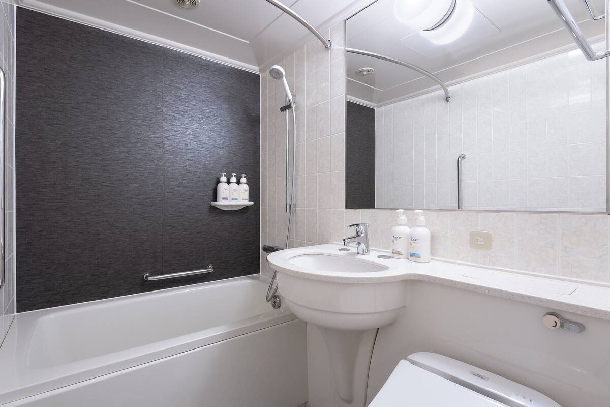 Une salle de bain moderne avec une baignoire, un lavabo et des toilettes. On peut voir deux bouteilles de savon Dove sur le lavabo.