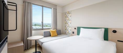 Et hotelværelse med seng, rundt bord, fjernsyn og et vindue med gardiner.
