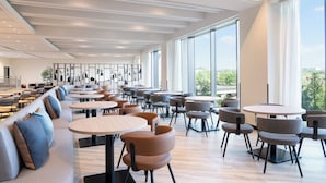 A spacious indoor area with multiple seating arrangements including round tables and sofas, large windows providing natural light, and a modern ceiling design. - ANA Holiday Inn Kobe Sanda by IHG (Sanda)