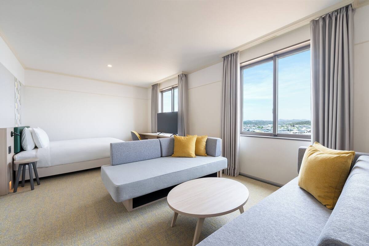 Une chambre d’hôtel moderne, dotée d’un canapé, d’une petite table, d’un bureau et offrant une vue sur la ville.
