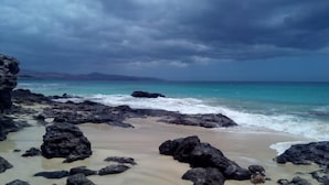 Una playa rocosa con olas rompiendo en la orilla bajo un cielo nublado.