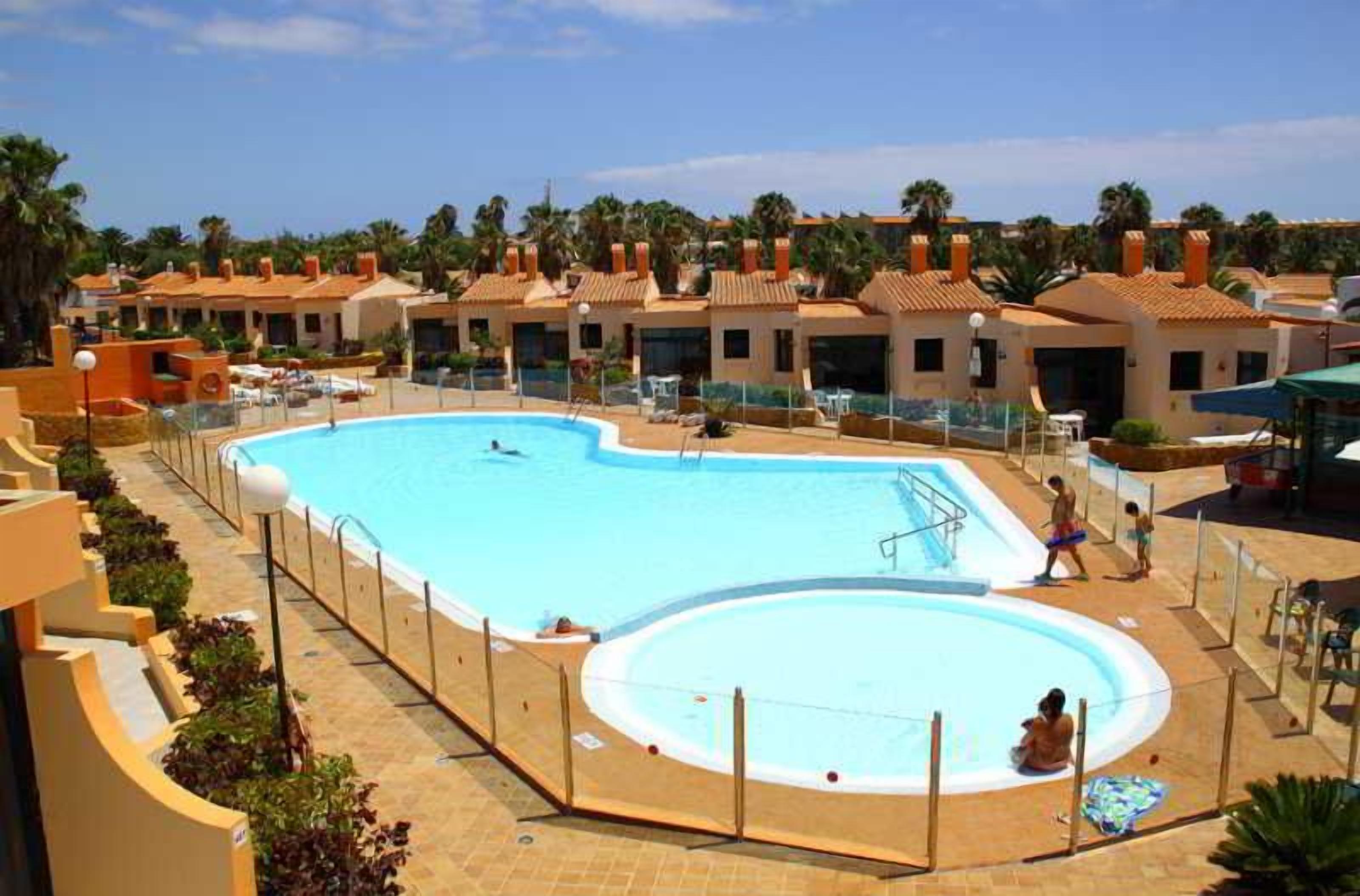 Piscina com área de solário, cercada por edifícios com telhados vermelhos.
