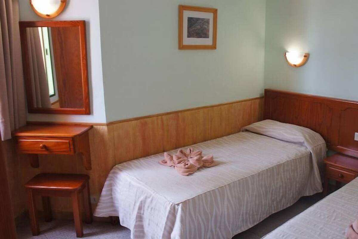 Hotellihuone, jossa on kaksi erillistä sänkyä, puinen yöpöytä, pieni työpöytä ja peili.