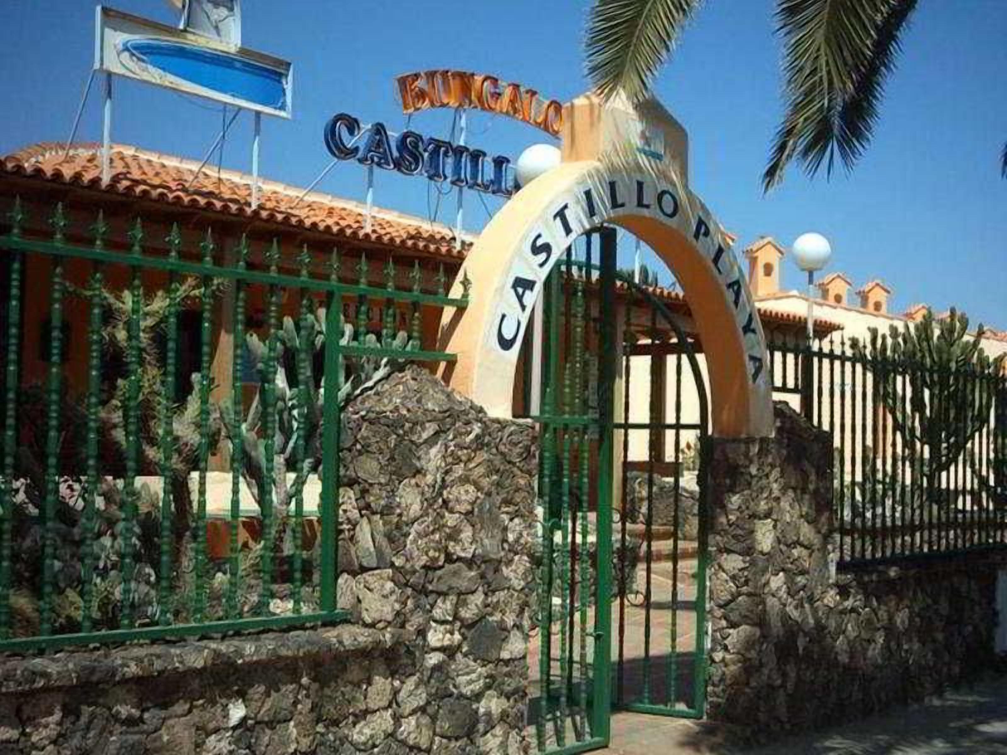 Una entrada protegida por un muro de piedra con cactus, y un cartel que dice 'Castillo Playa'.