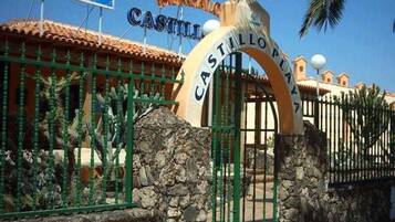 Una entrada protegida por un muro de piedra con cactus, y un cartel que dice 'Castillo Playa'.